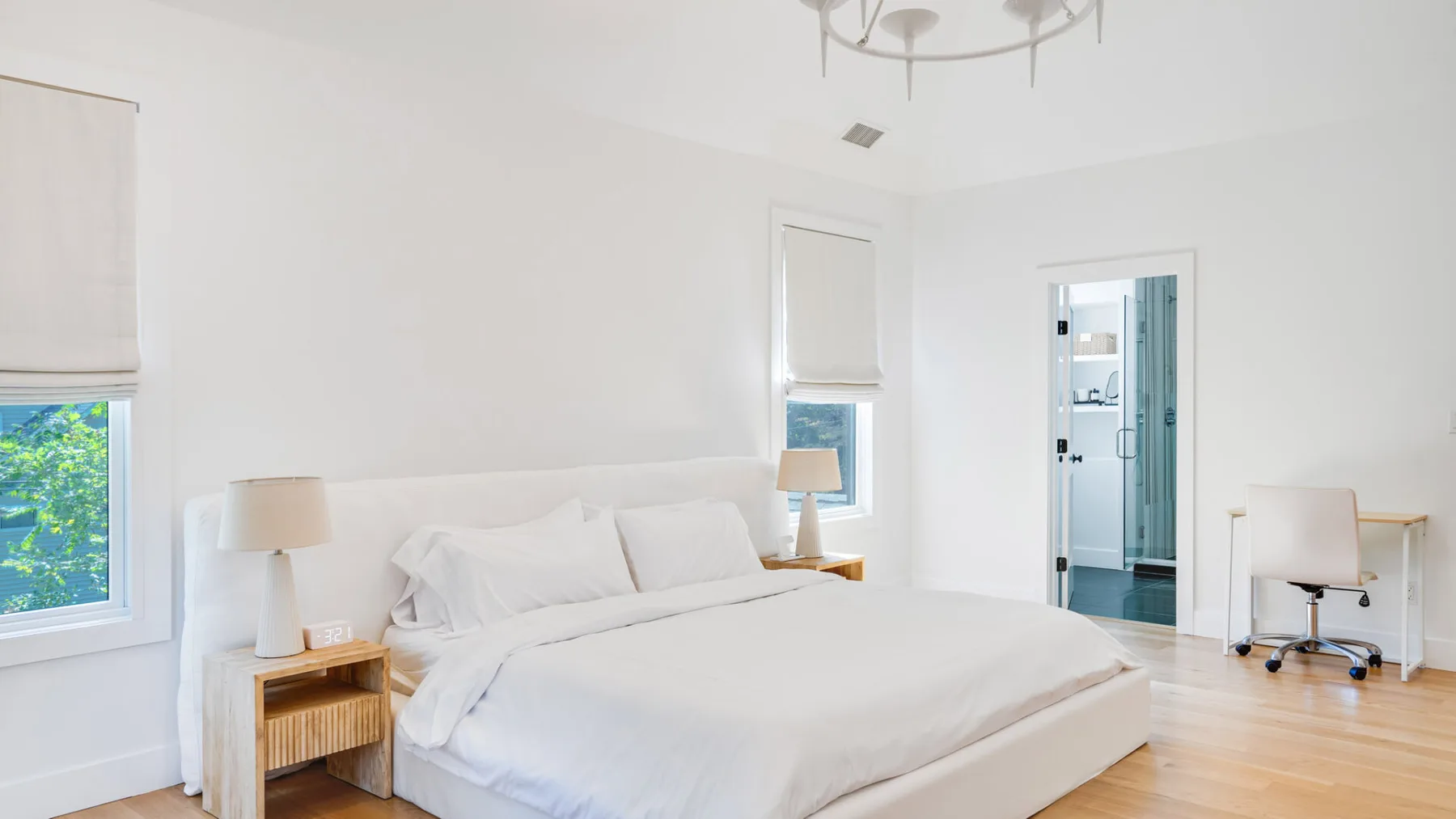 A bright bedroom with a large bed, bedside tables, and a desk by the doorway.
