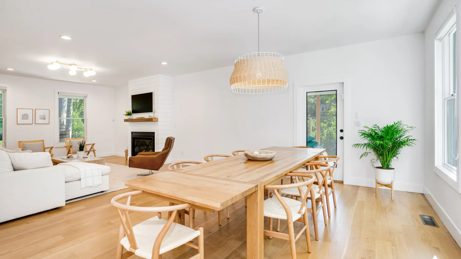 A bright open-plan dining and living area with a long wooden table and white seating.