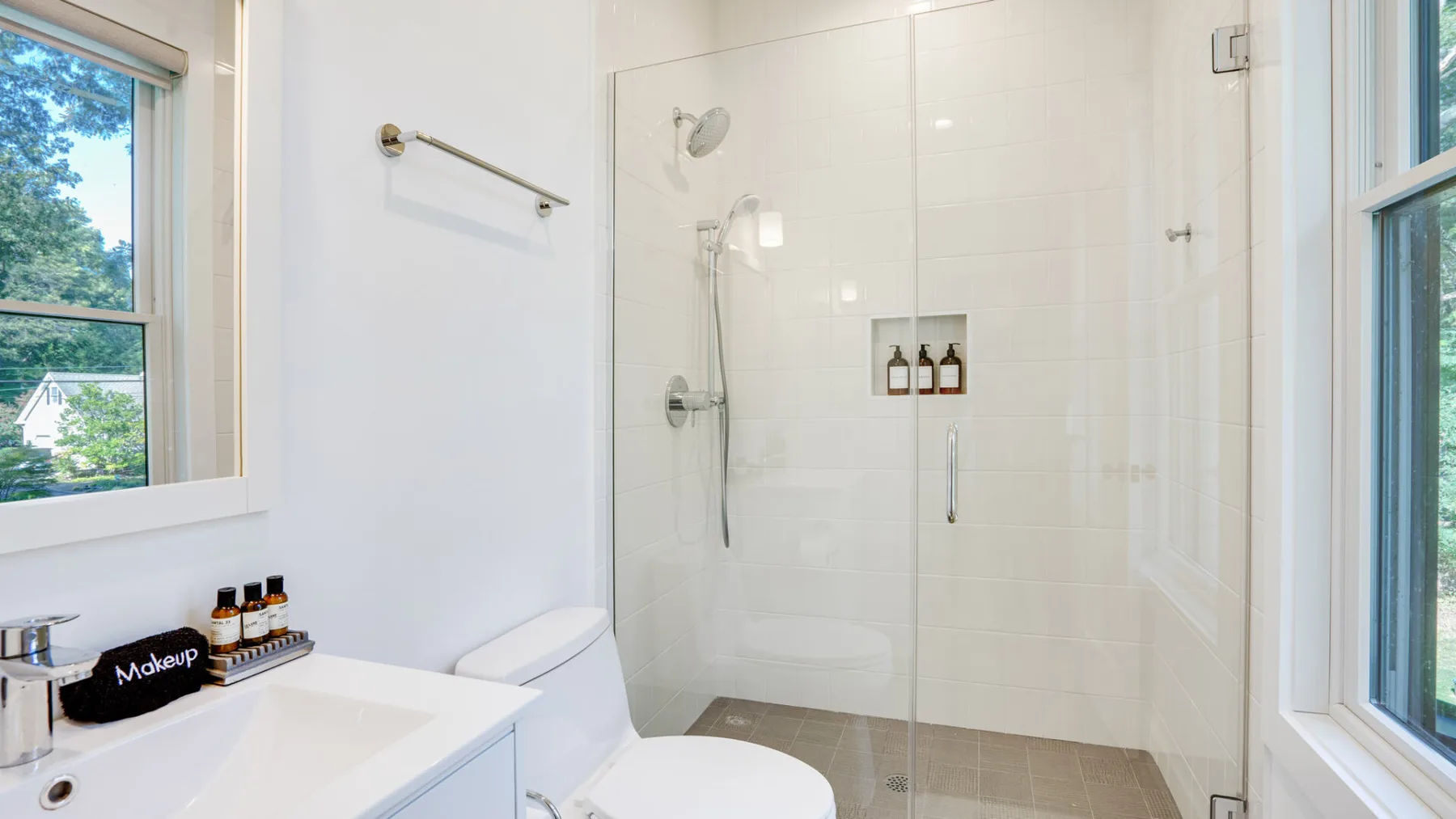 A bright bathroom with a glass shower and a sink beside a window.
