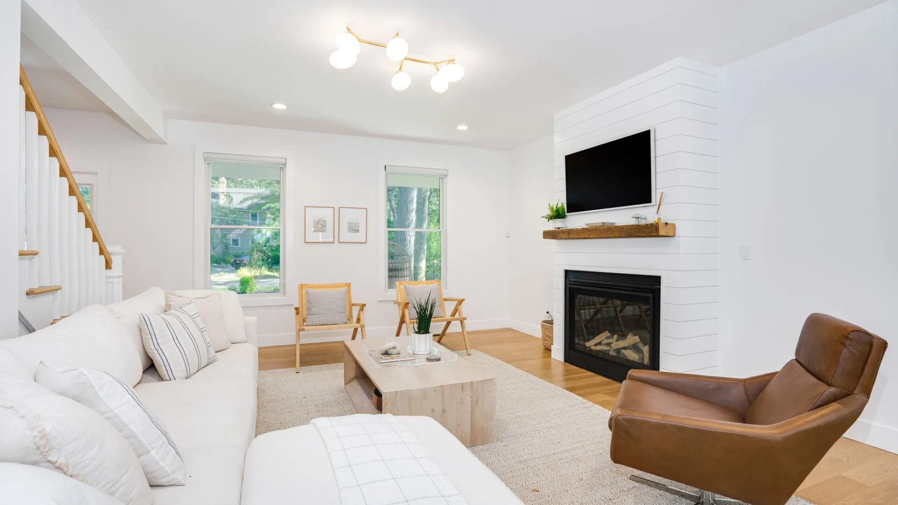 A bright living room with white seating, a fireplace, and large windows.