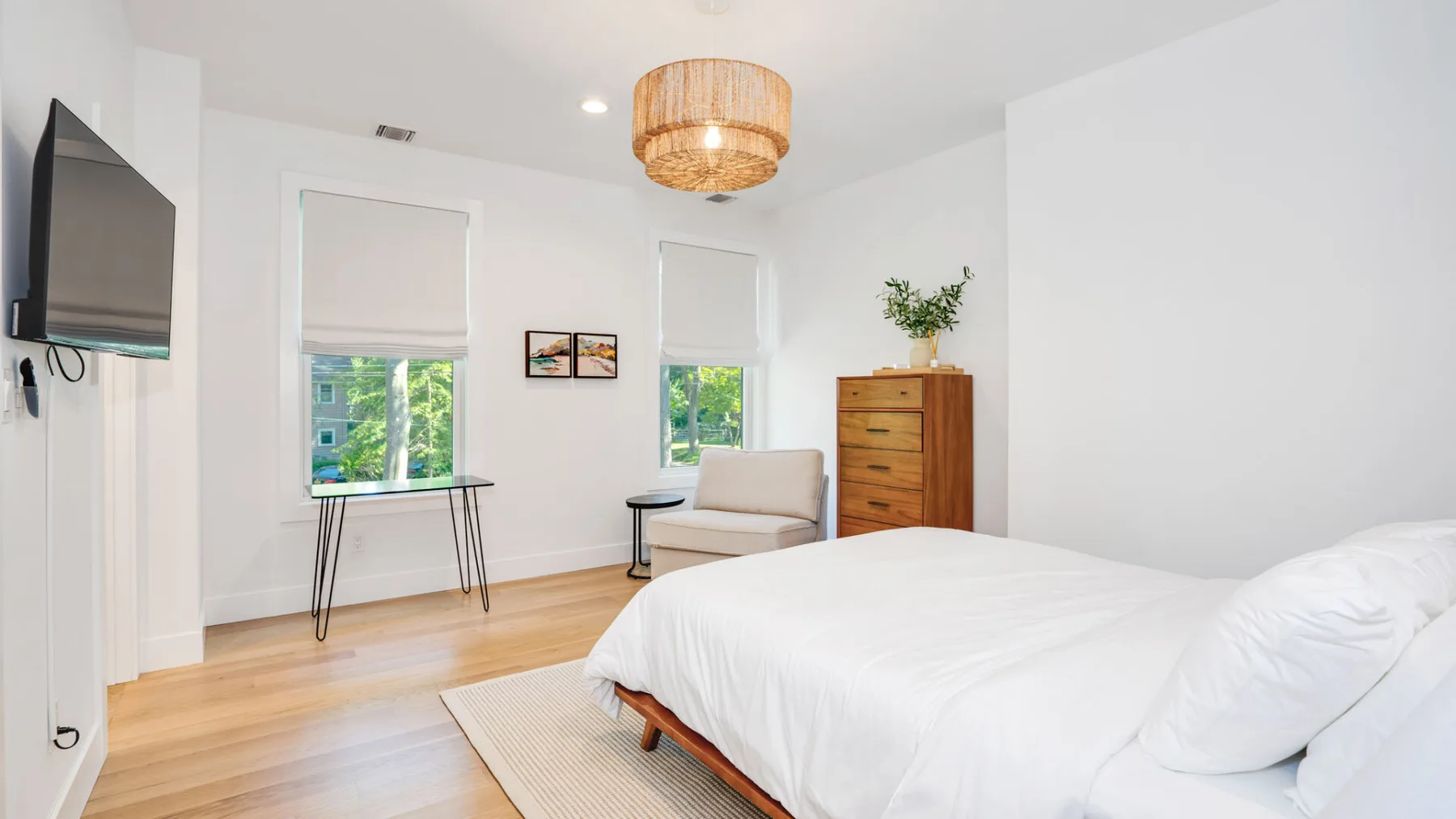 A bright bedroom with a bed, a small seating area, and windows.