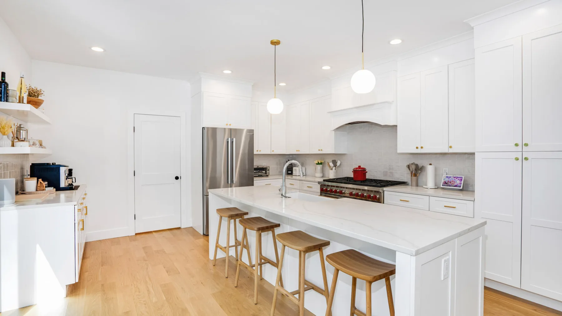 A bright white kitchen with a large island and wooden stools.