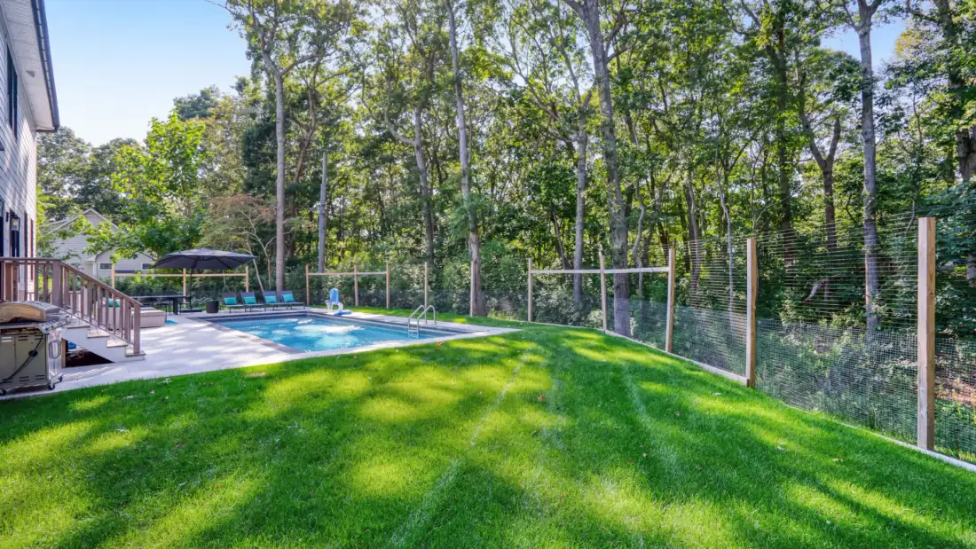 A backyard with a swimming pool, green lawn, and trees.