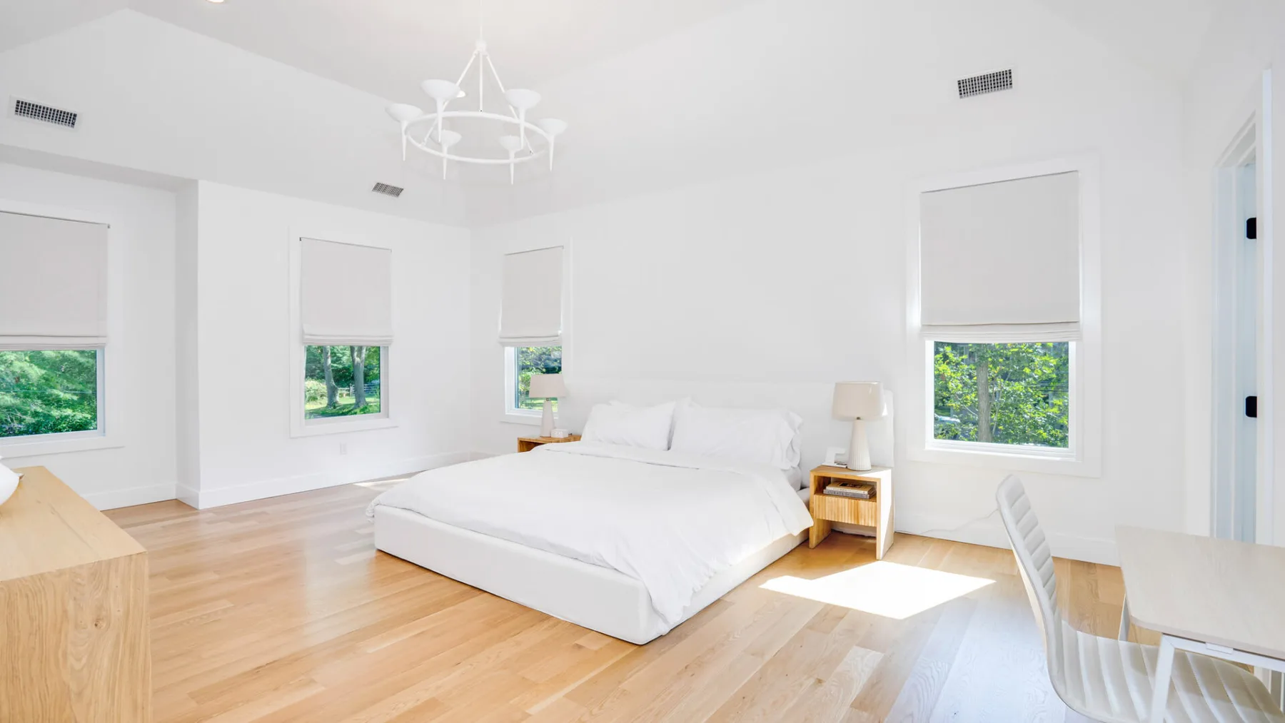 A bright bedroom with a white bed and several windows.