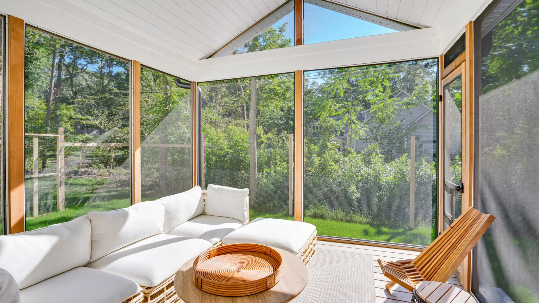 A bright enclosed sunroom with large windows and white seating.
