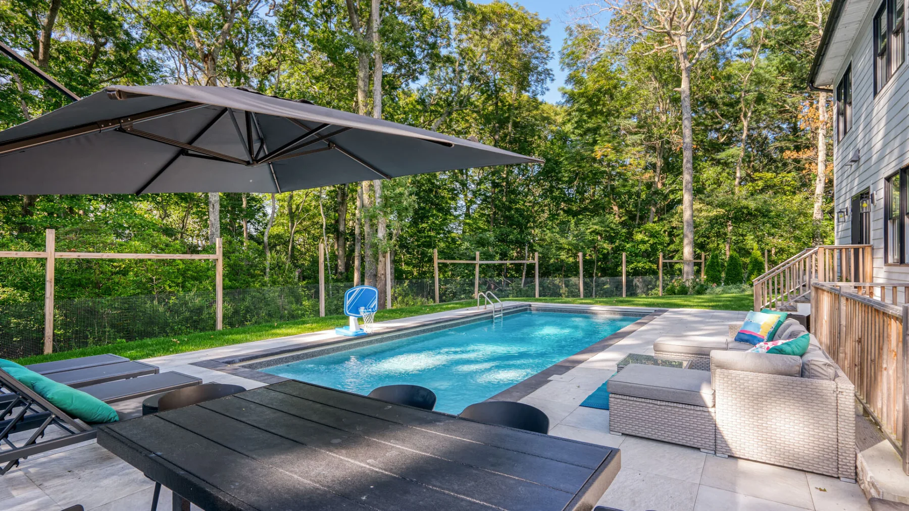 An outdoor swimming pool beside a deck with seating and a large umbrella.