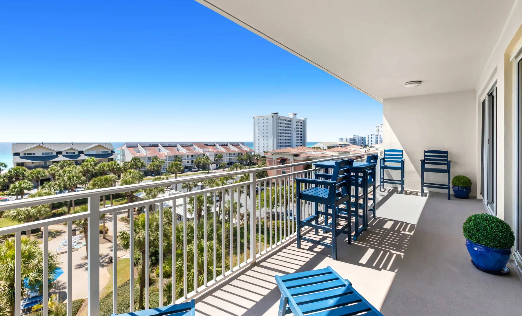 A covered balcony with blue seating overlooks palm trees and nearby buildings.