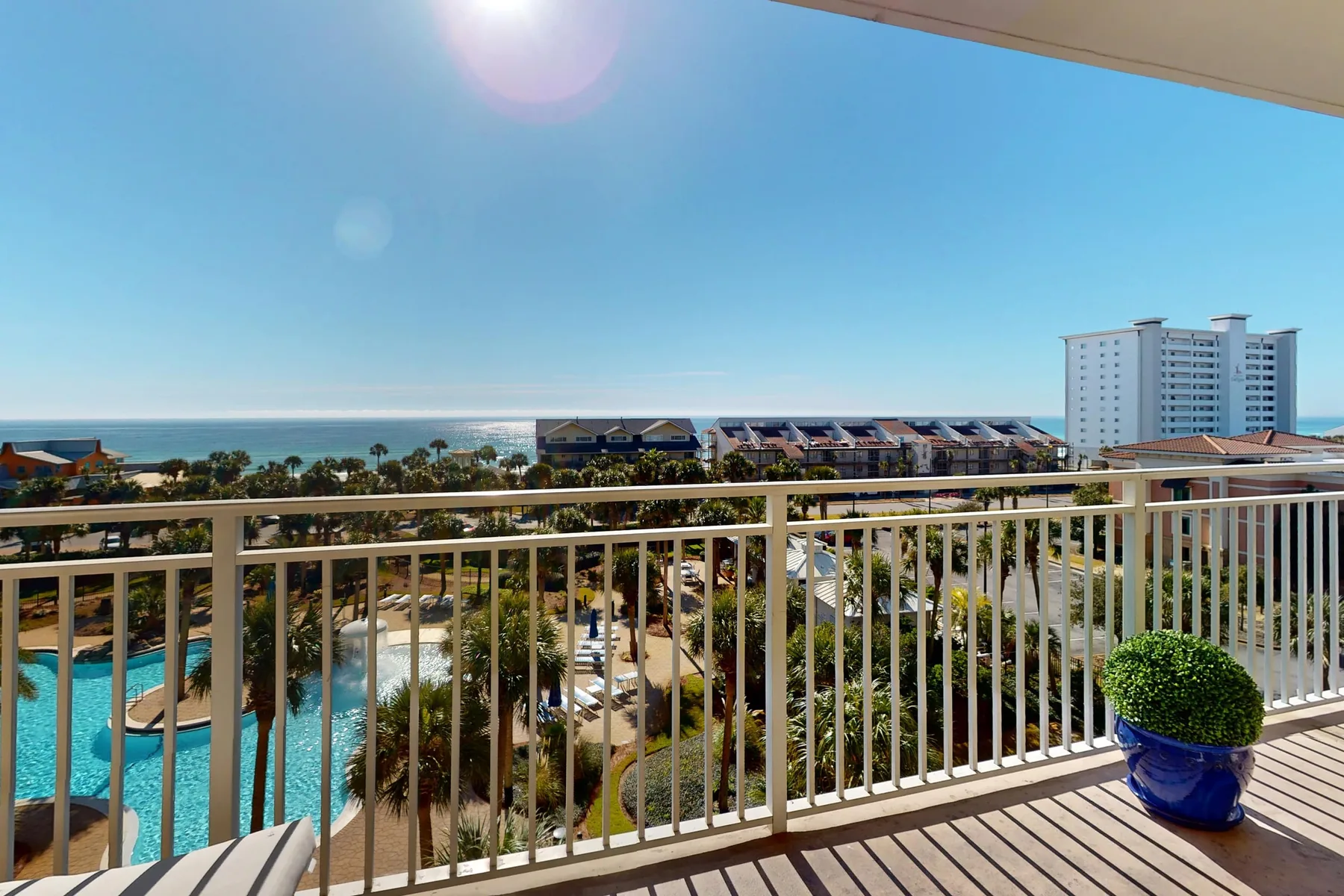 A balcony overlooks a landscaped resort, with the sea visible beyond the buildings.
