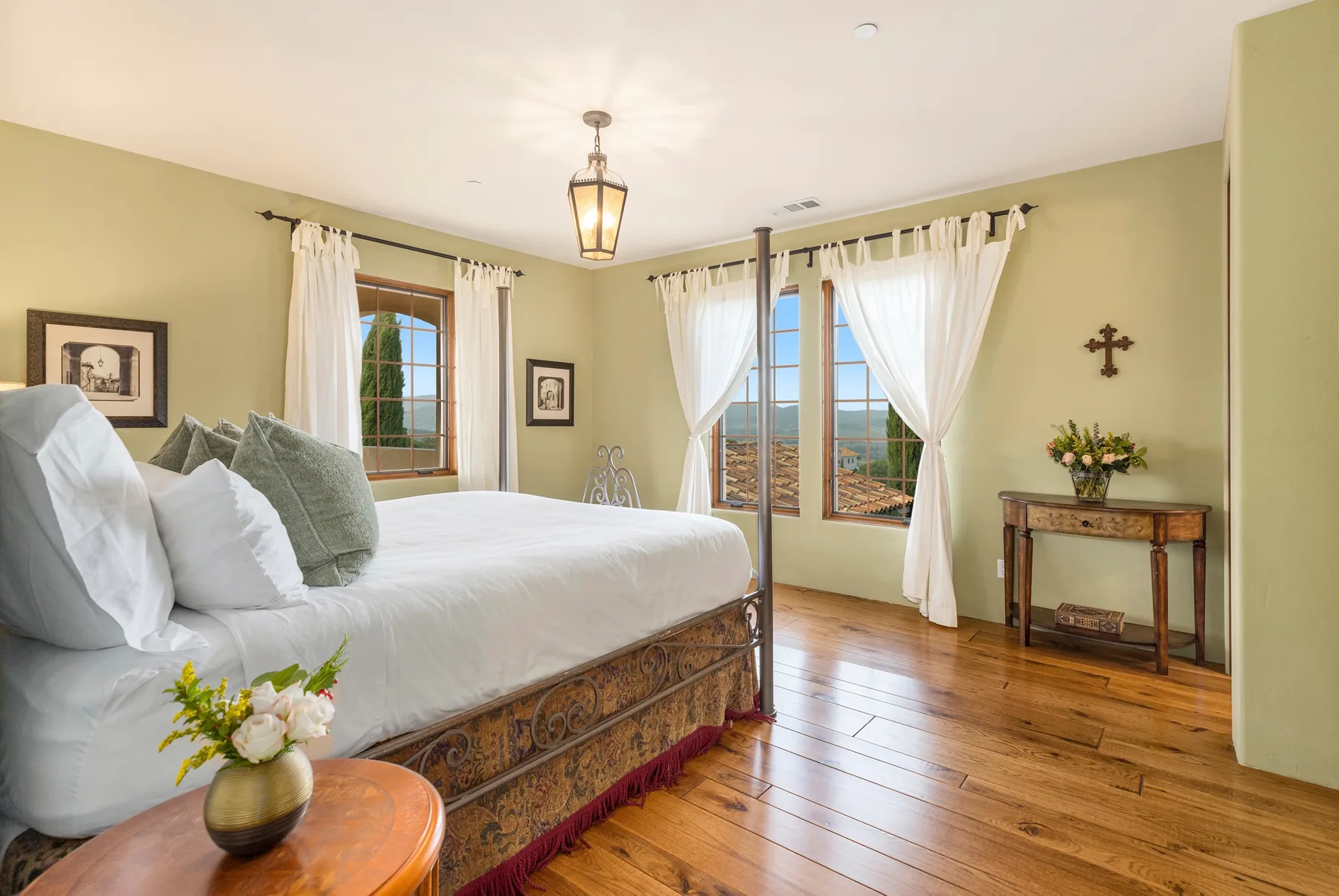 Un dormitorio con una cama grande, ventanas con cortinas y piso de madera.