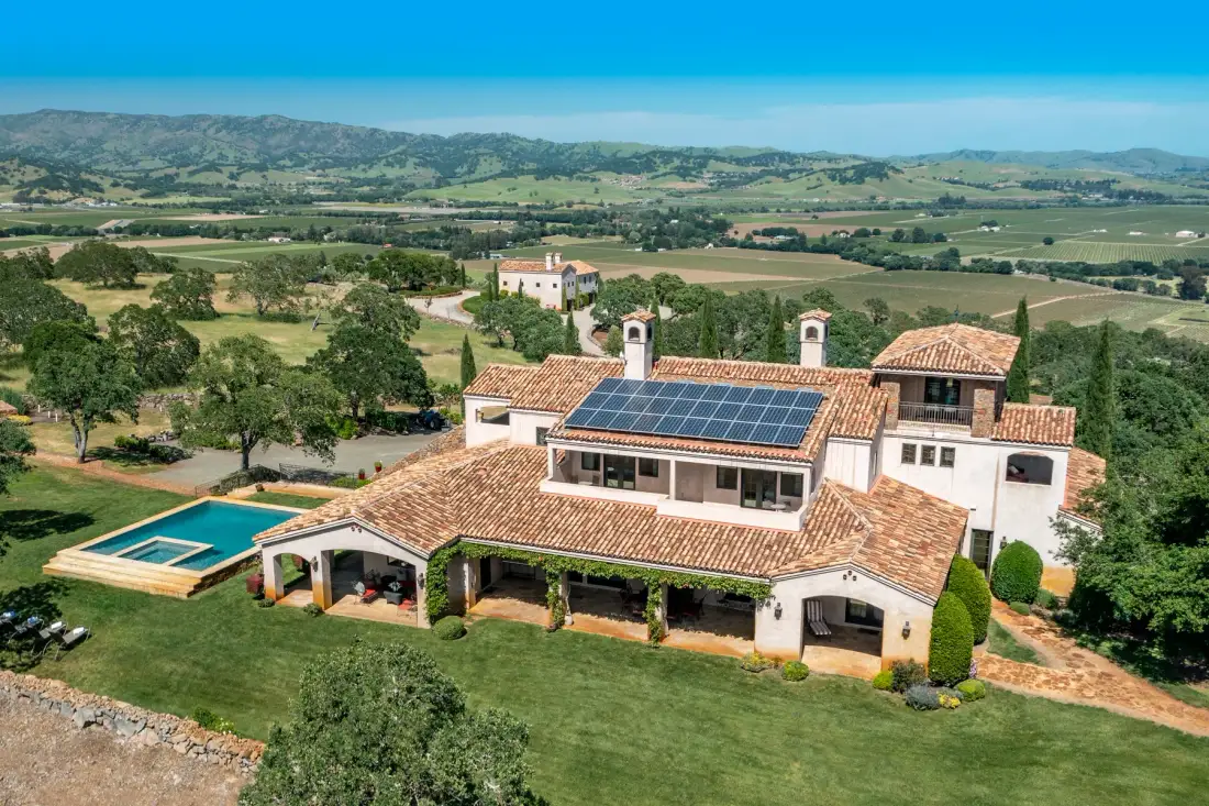 Una gran casa en el campo, con tejado de tejas y paneles solares, domina campos ondulados.