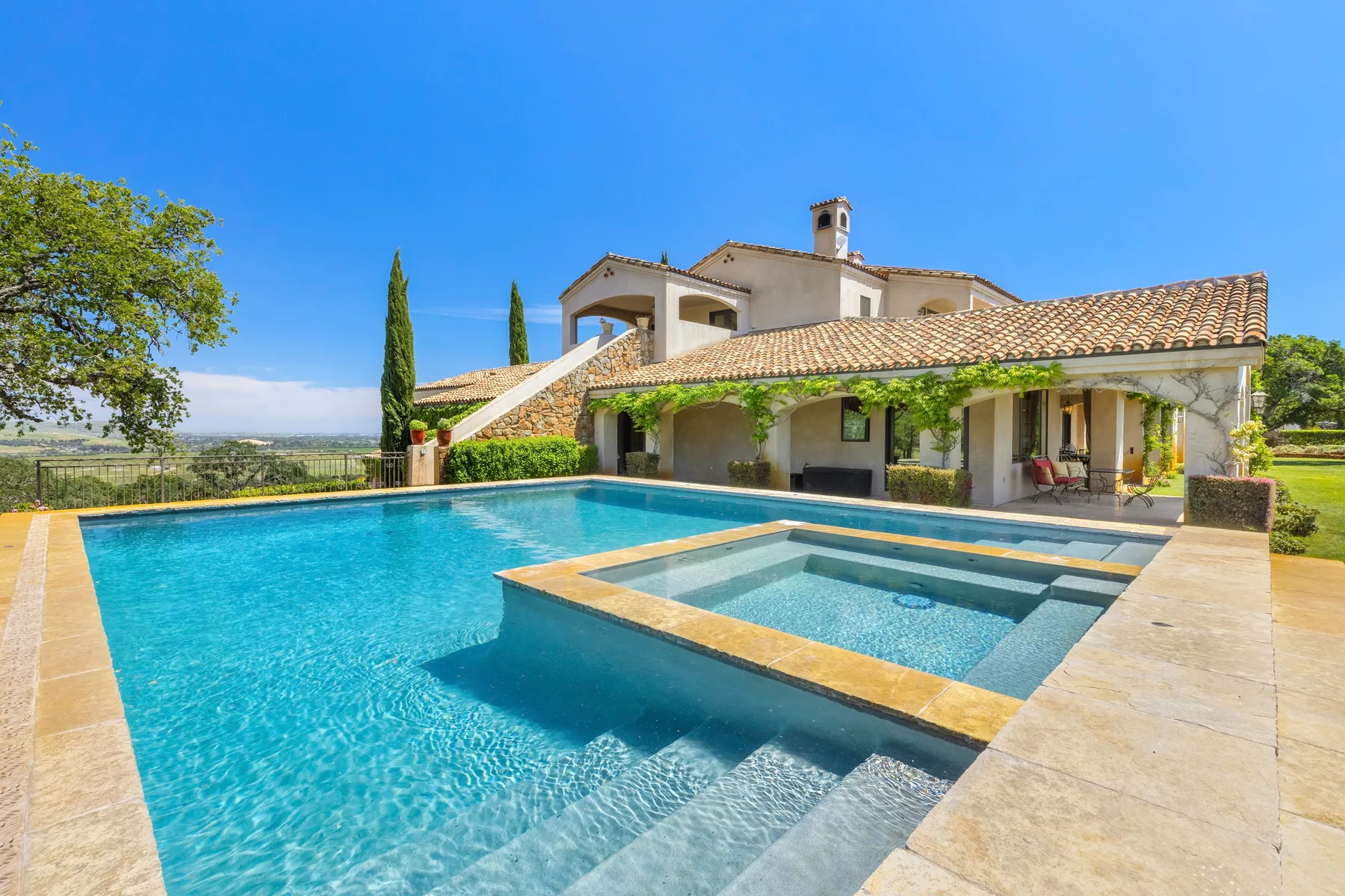 Piscina exterior y zona de poca profundidad junto a una casa con techo de tejas.