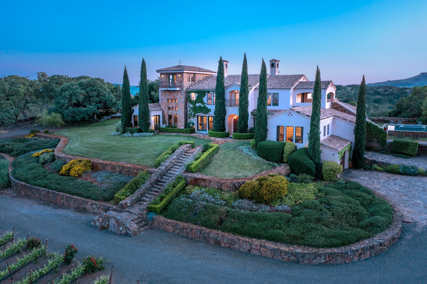 Una gran casa de campo se alza entre jardines y altos cipreses.