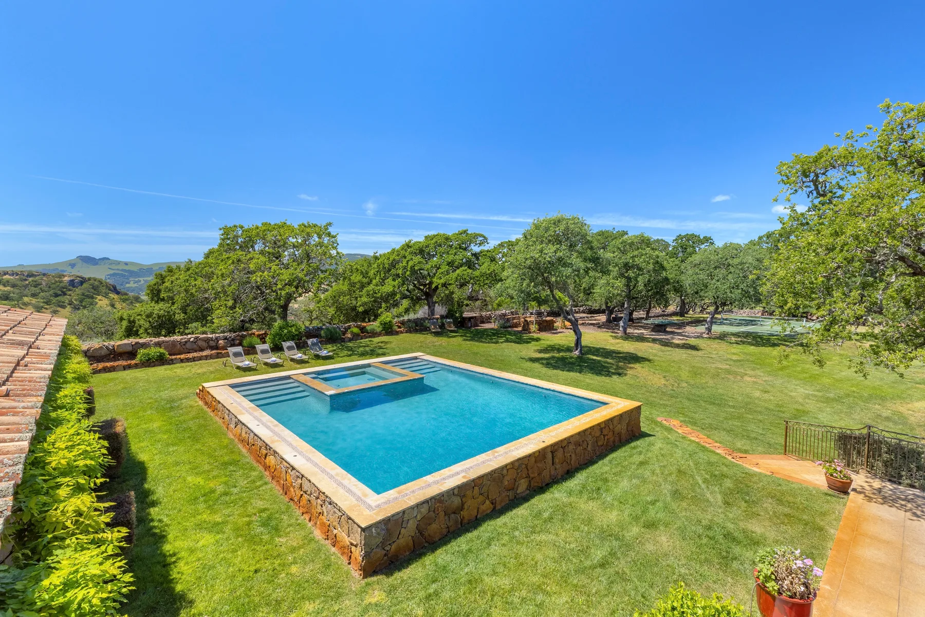 Una piscina al aire libre se encuentra en un jardín con césped y árboles.