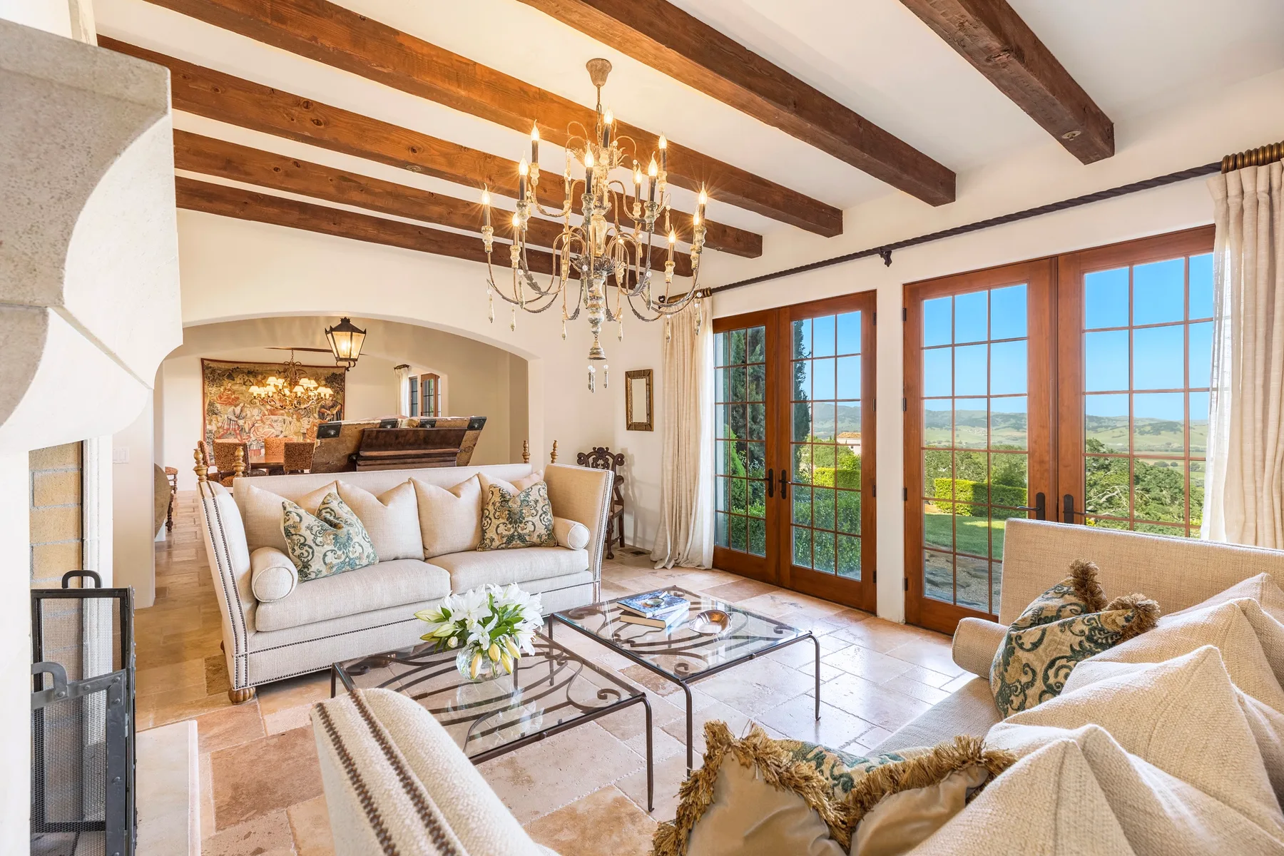 A bright living room with seating, a chandelier, and glass doors opening onto a view.