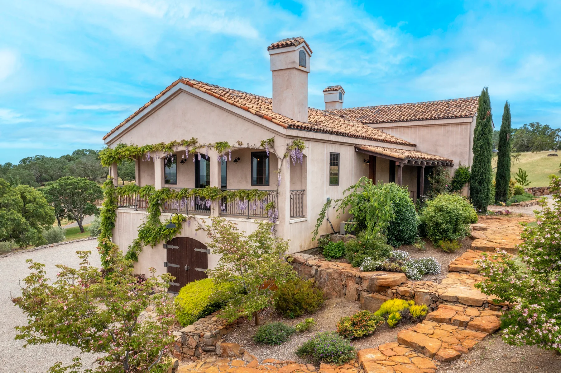 Vista exterior de una casa estucada con techo de tejas, jardín y sendero de piedra.