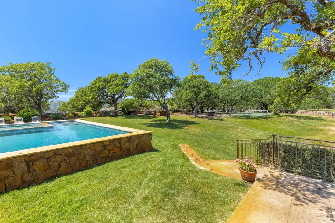 Un jardín con piscina, césped y árboles maduros.