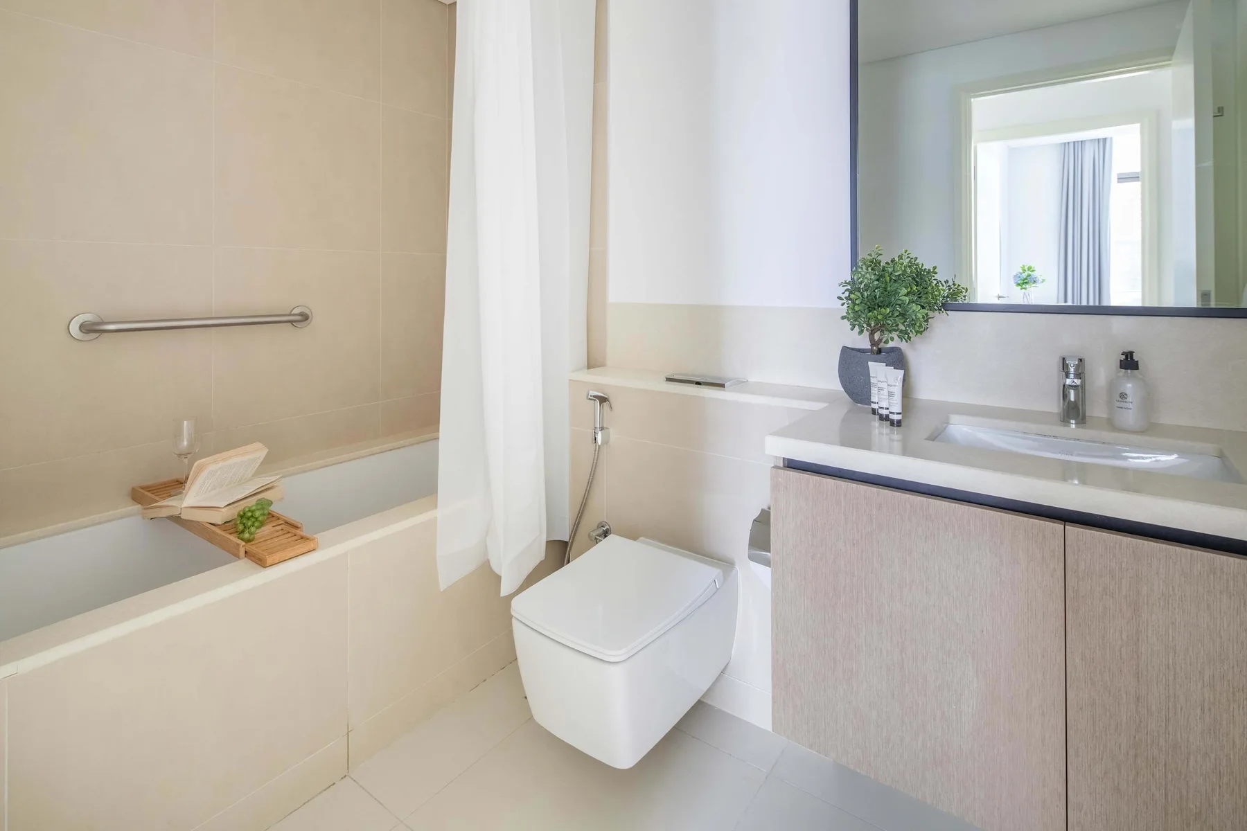 Un baño luminoso con bañera, cortina de ducha, inodoro suspendido y lavabo con mueble.