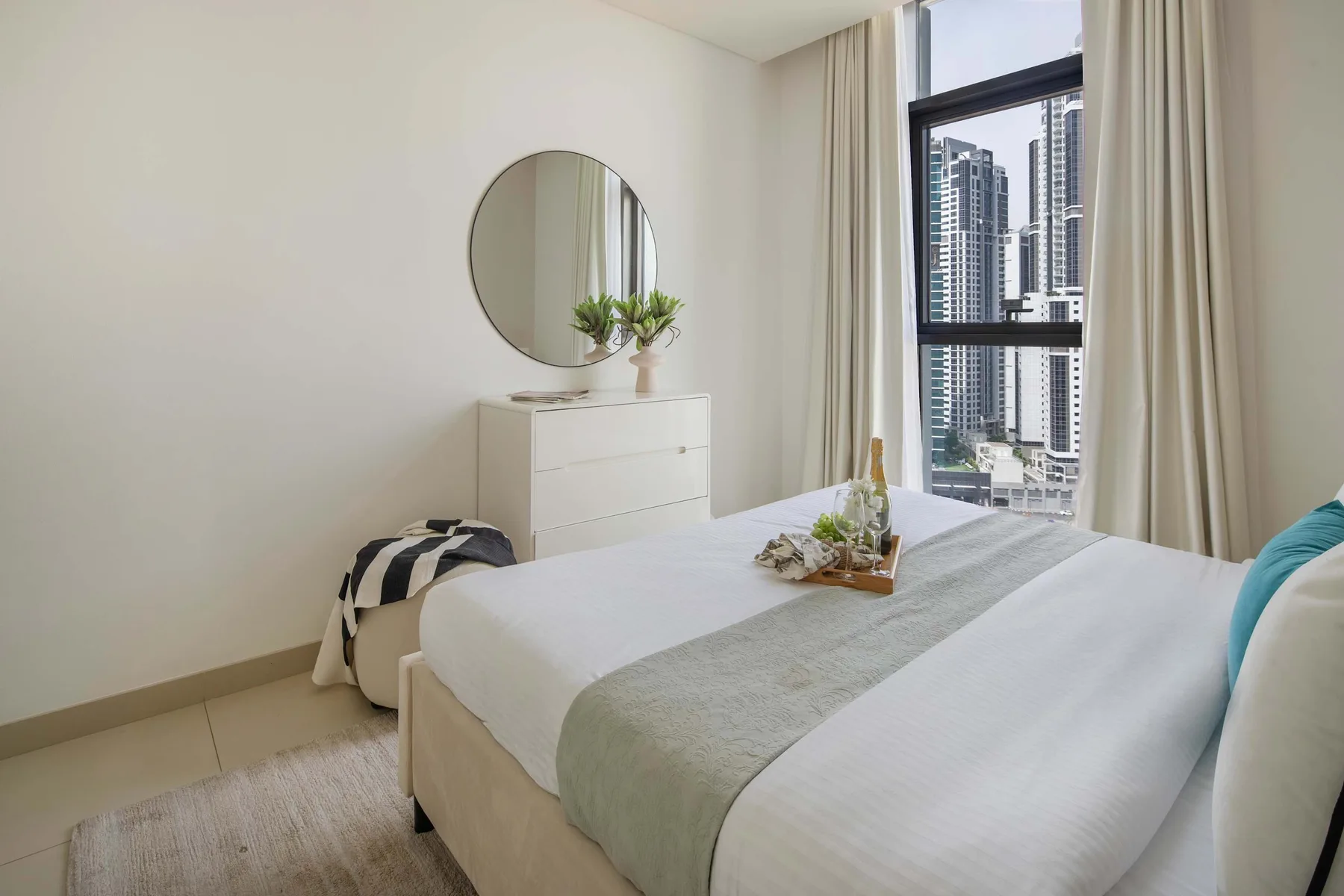 Un dormitorio luminoso con una cama bien tendida junto a una ventana alta.