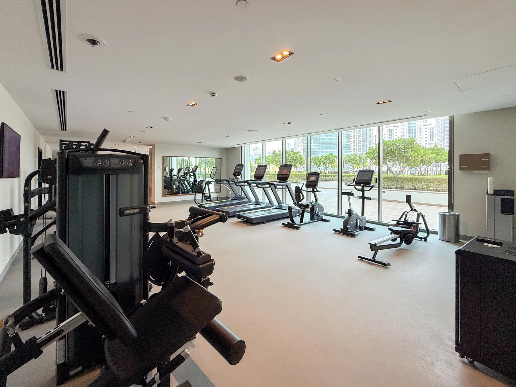 Un gimnasio luminoso con máquinas de ejercicio y grandes ventanas frente a zonas verdes.