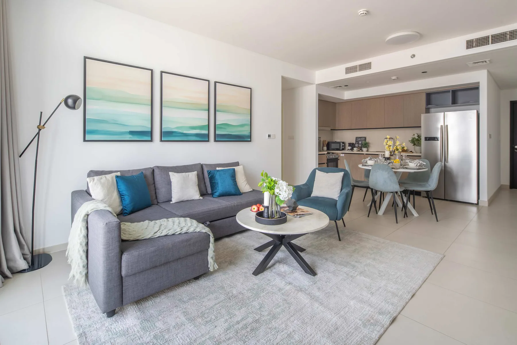 Una sala luminosa con un sofá seccional gris y una cocina-comedor abierta.