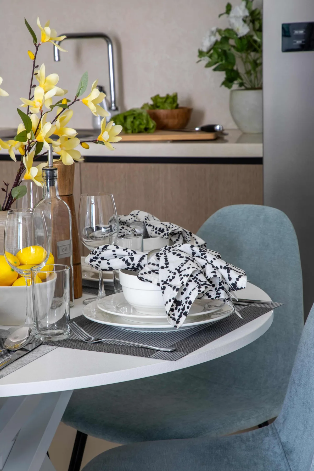 Una mesa de comedor está puesta con platos, vasos y un paño estampado junto a la cocina.