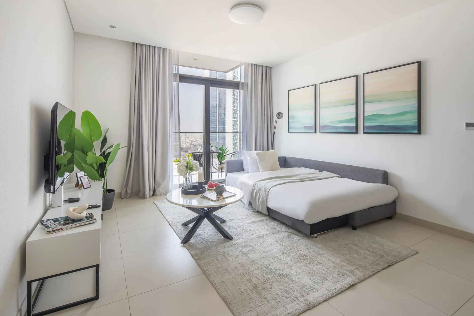 Un dormitorio luminoso con una cama, cuadros enmarcados y una zona de estar junto a la ventana.