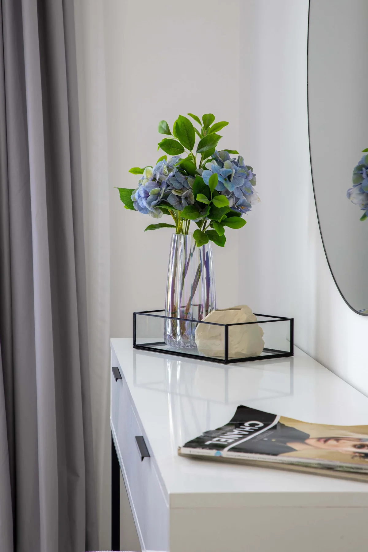 Un rincón luminoso con una consola blanca, flores y una revista.