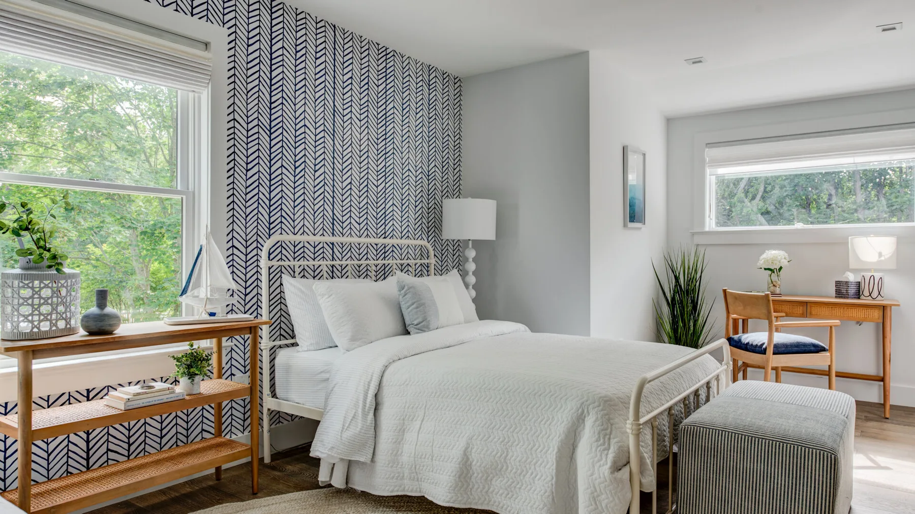 Un dormitorio luminoso con una cama, una pared decorativa estampada y ventanas grandes.