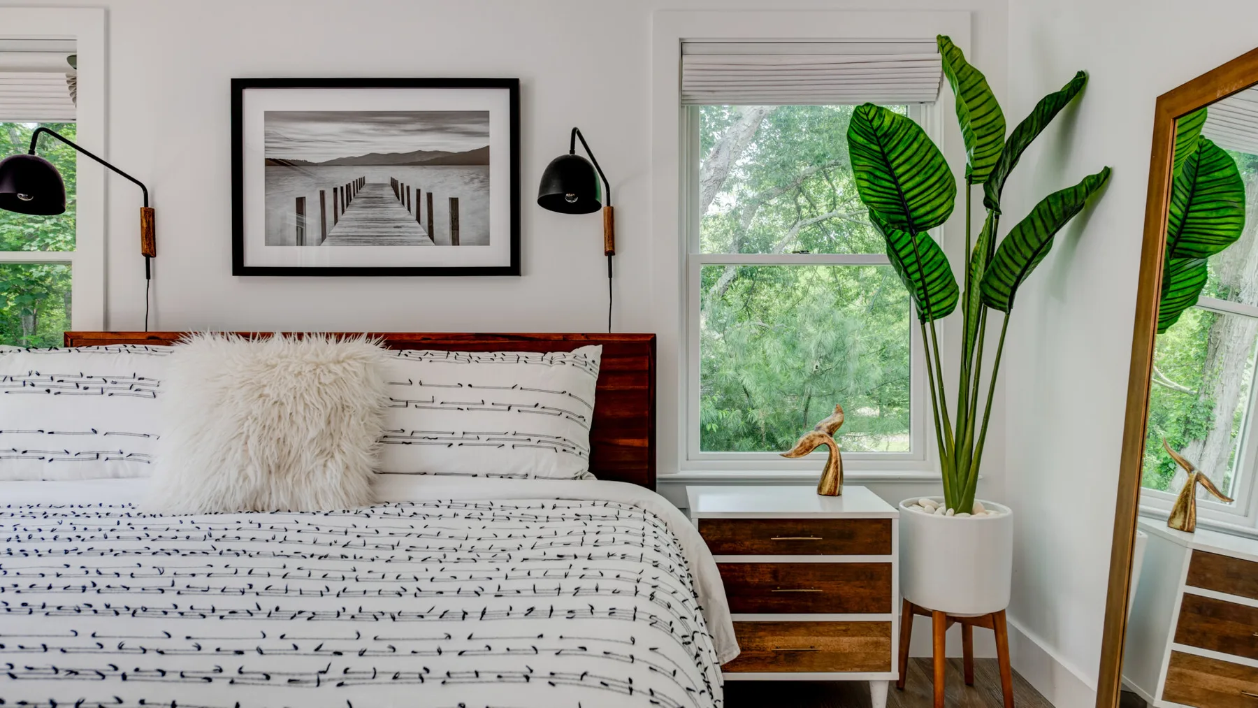 Un dormitorio con una cama tendida, una planta frondosa y una ventana grande.