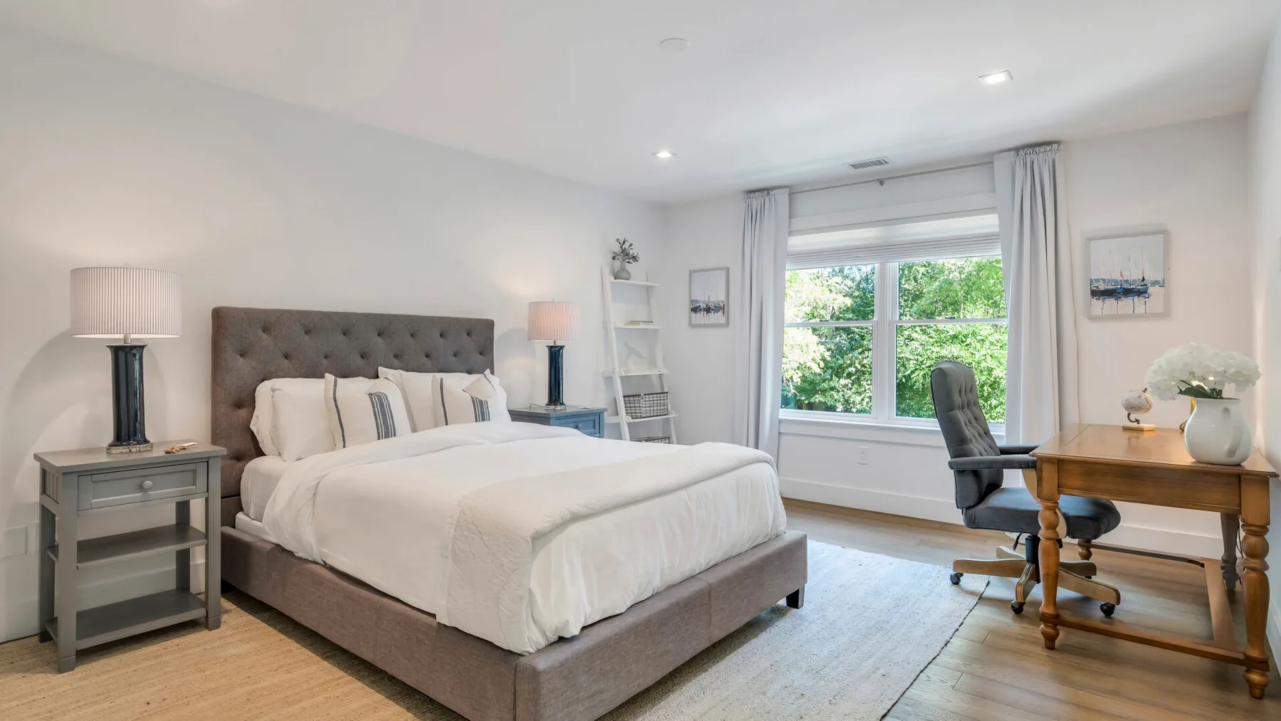 Un dormitorio luminoso con una cama arreglada y un escritorio junto a la ventana.