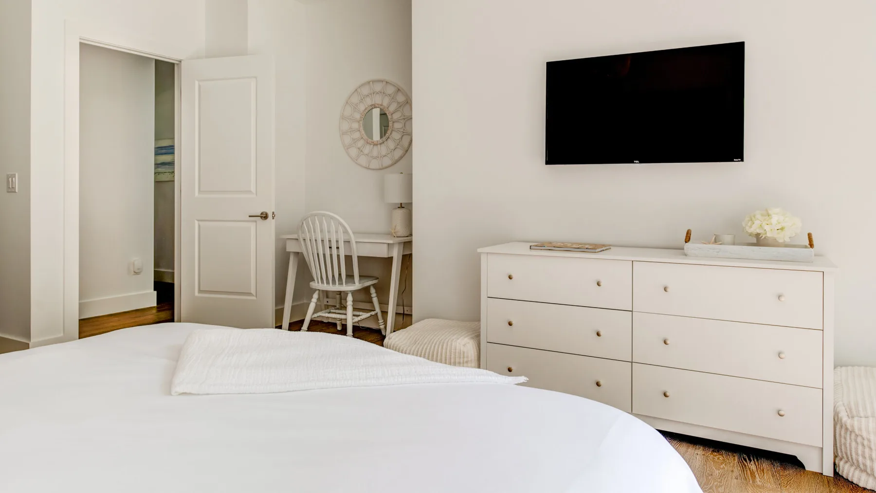 Un dormitorio luminoso con una cama, una cómoda y un televisor en la pared.