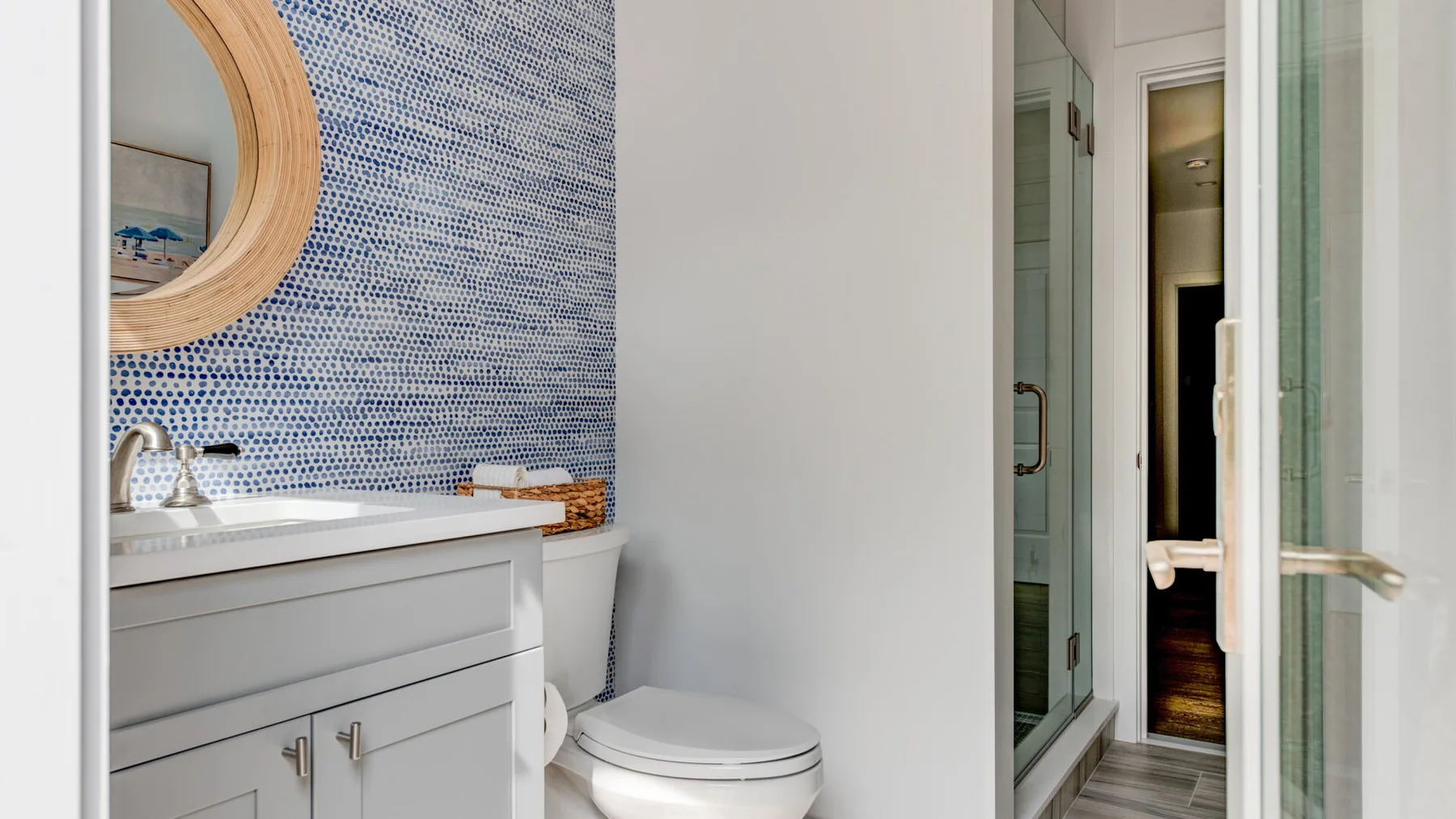 Un tocador y un inodoro están junto a una ducha de vidrio con mosaicos azules.
