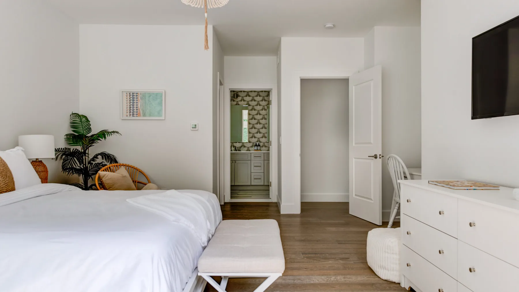 Un dormitorio luminoso con una cama tendida, una cómoda y una puerta abierta.