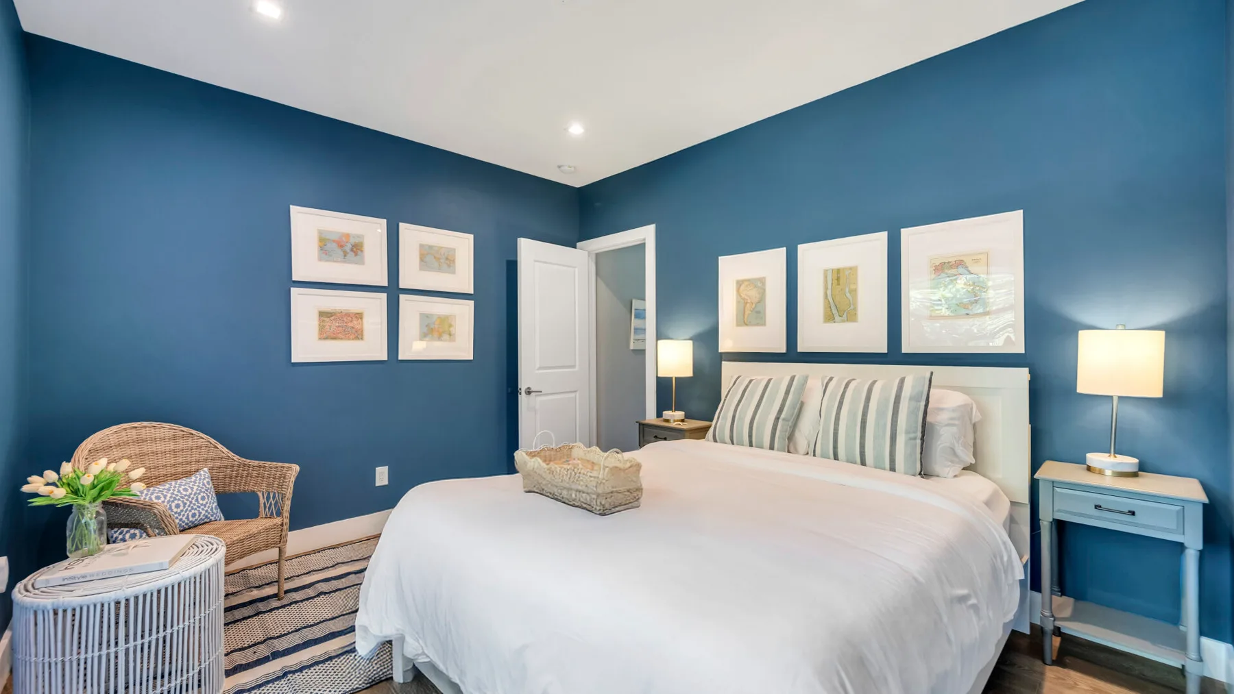 Un dormitorio con una cama bien tendida y cuadros en las paredes azules.