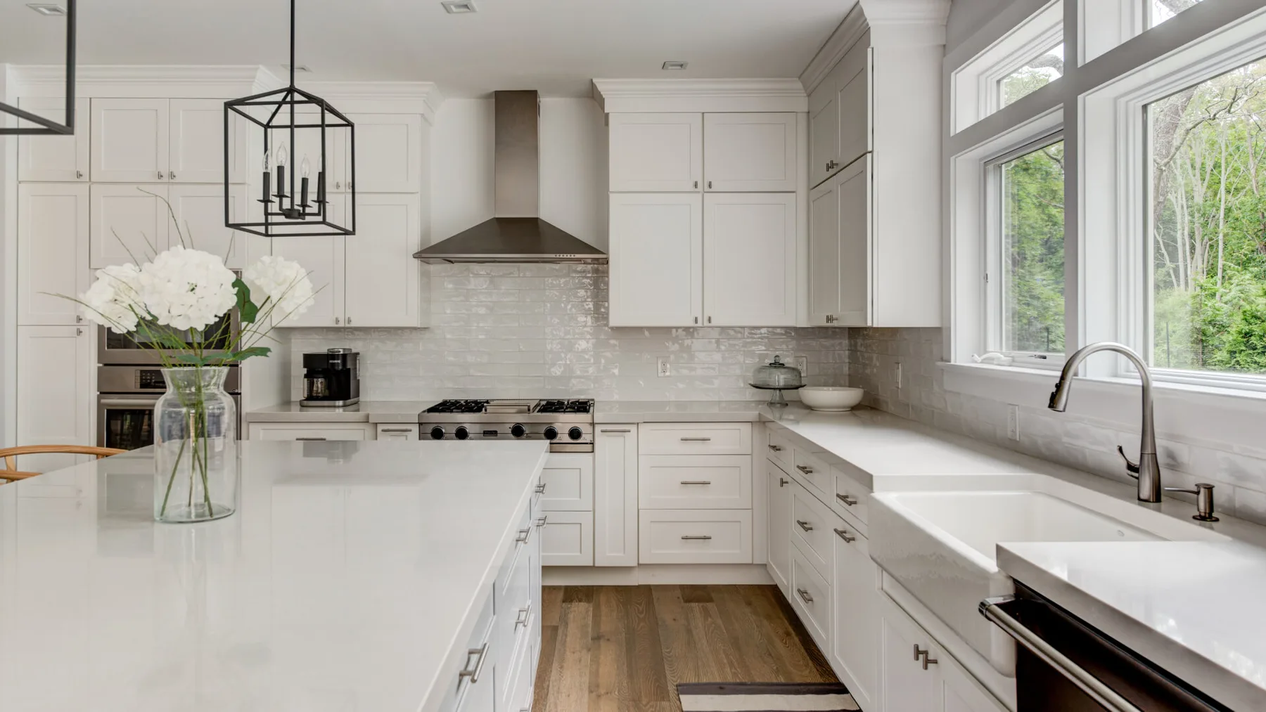 Una cocina blanca y luminosa con isla central, estufa de acero inoxidable y grandes ventanas.