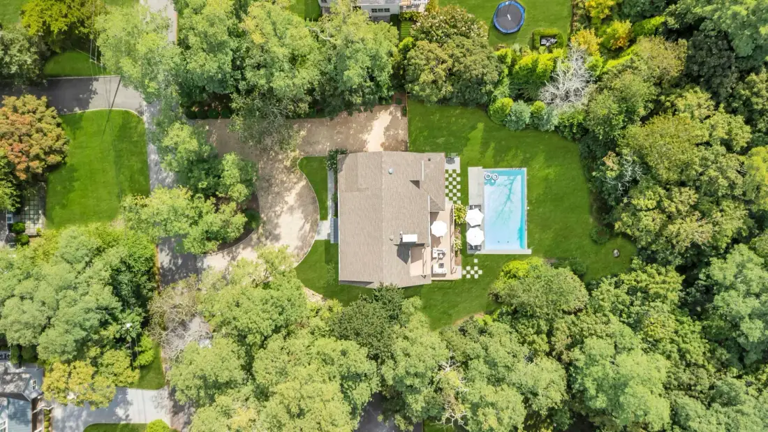 Vista aérea de una casa rodeada de árboles, con una piscina cercana.