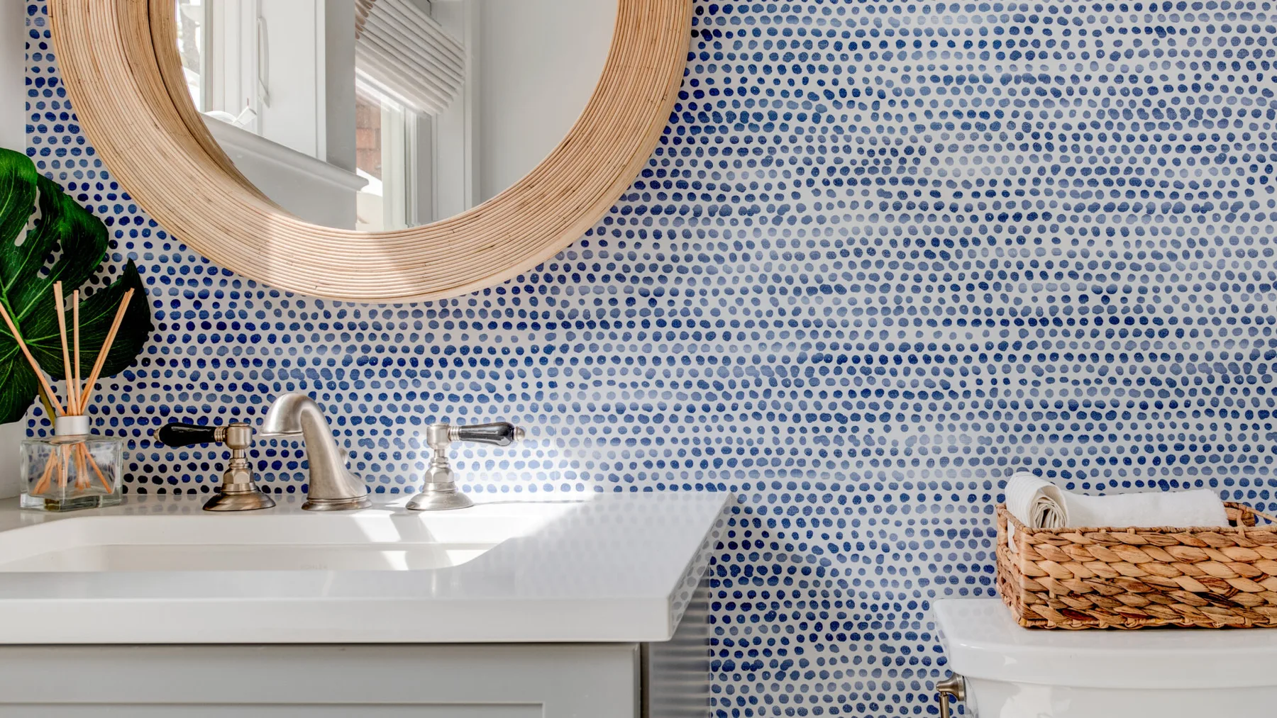 Un lavabo de baño con espejo redondo frente a una pared de azulejos azules y blancos.