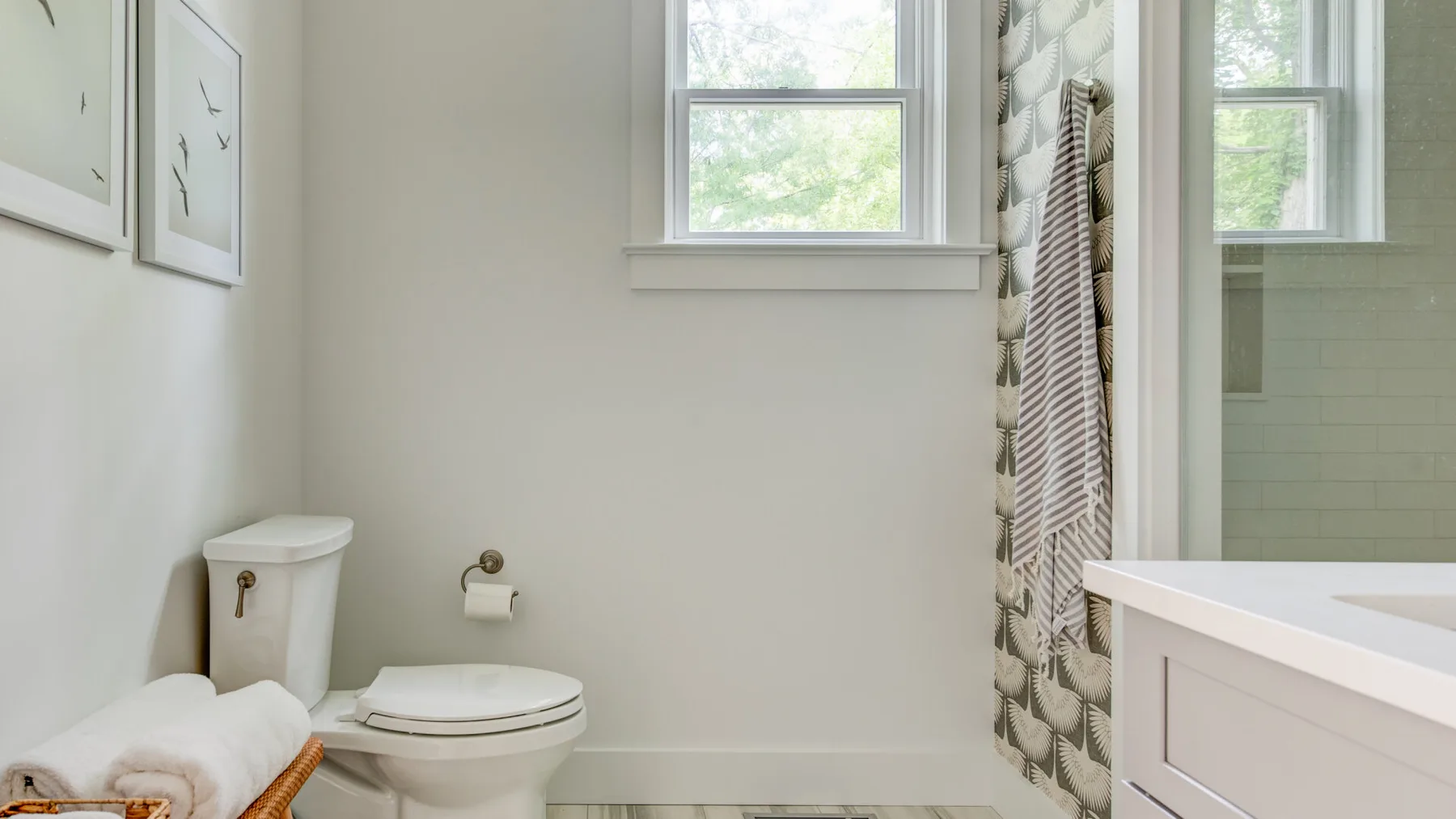 Un baño con inodoro, lavabo y cortina de ducha estampada junto a una ventana.