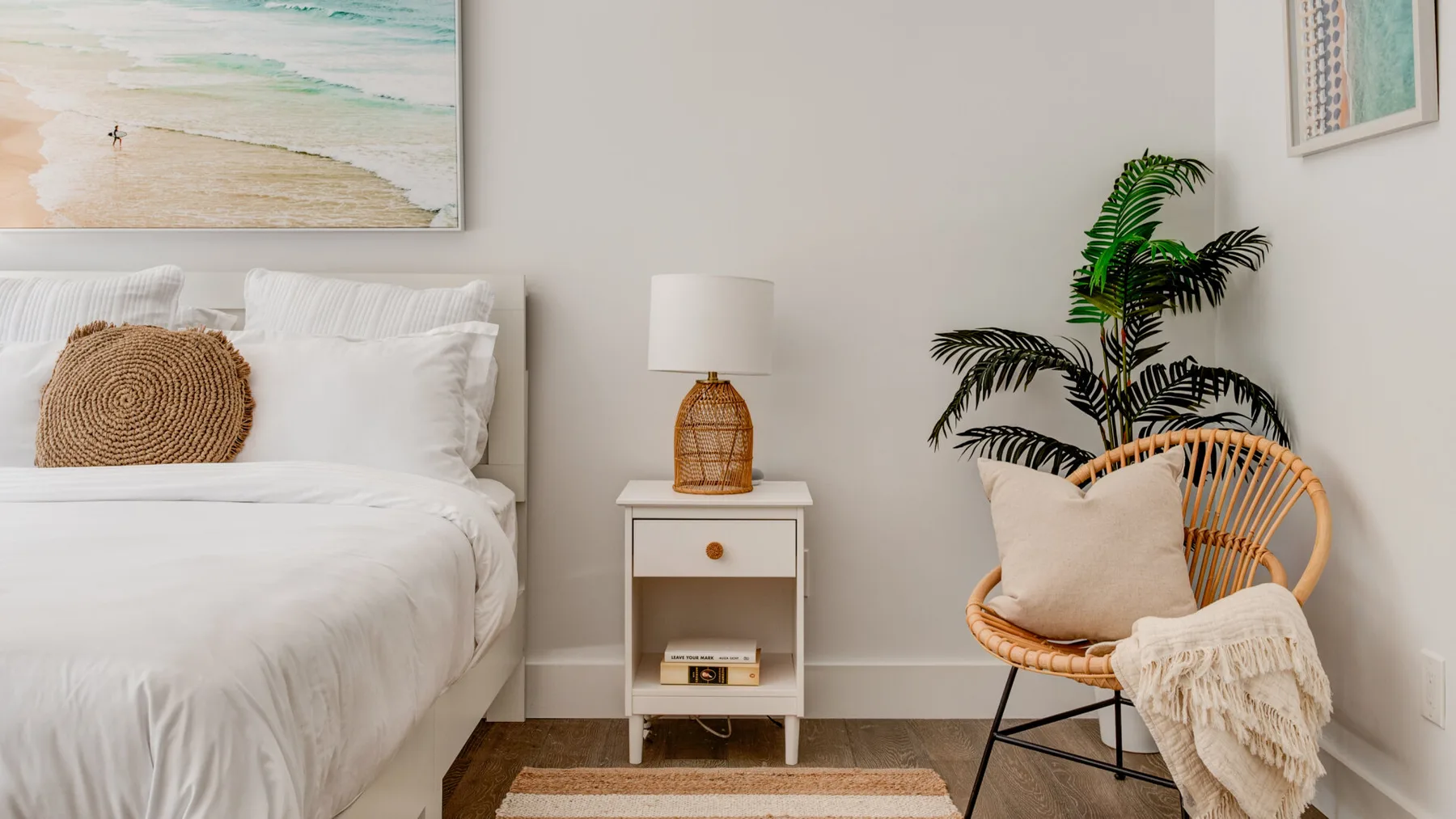 Un dormitorio con una cama blanca, una mesita de noche y una silla tejida.