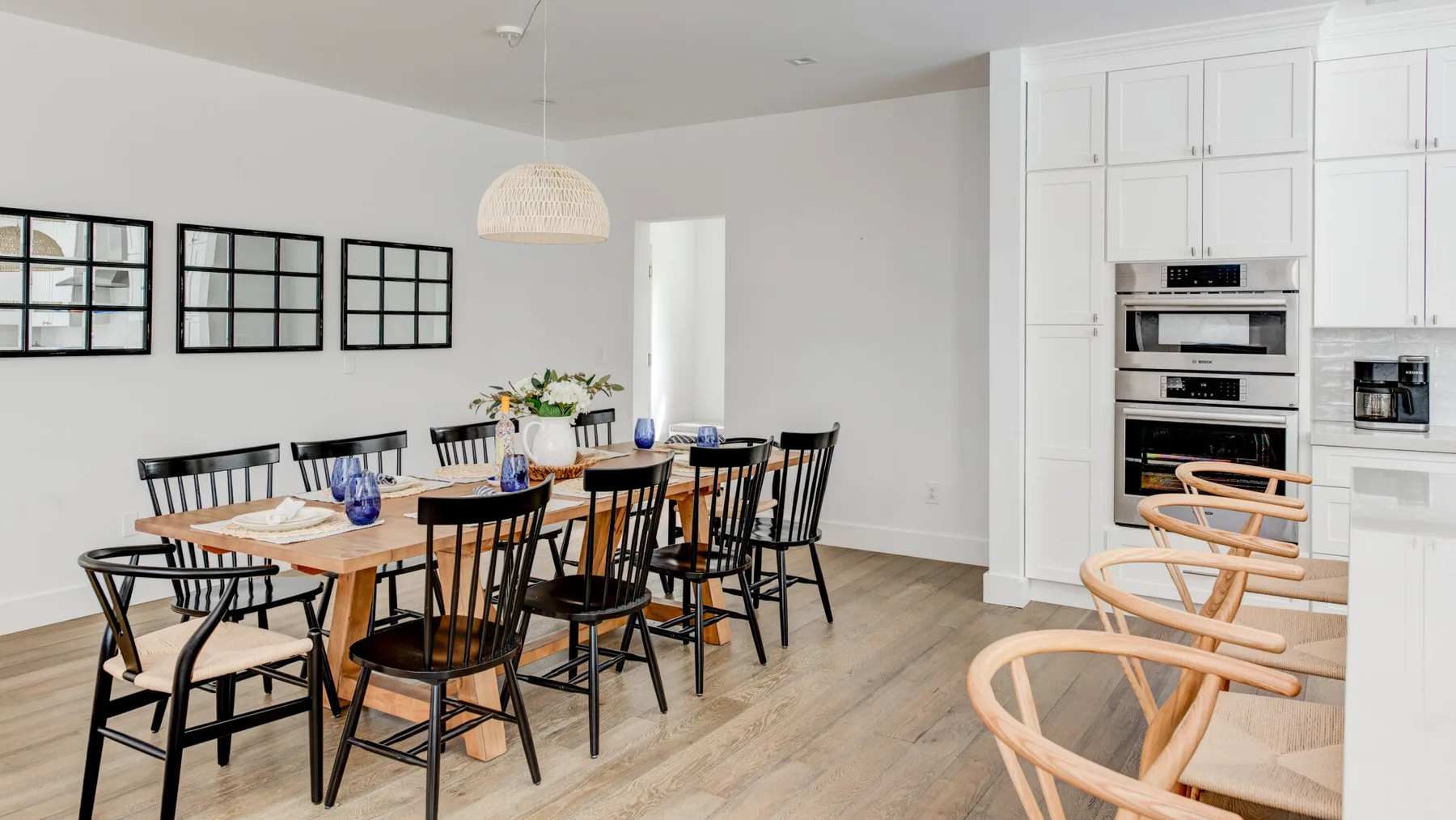 Comedor con una mesa larga de madera y asientos negros junto a una cocina blanca.