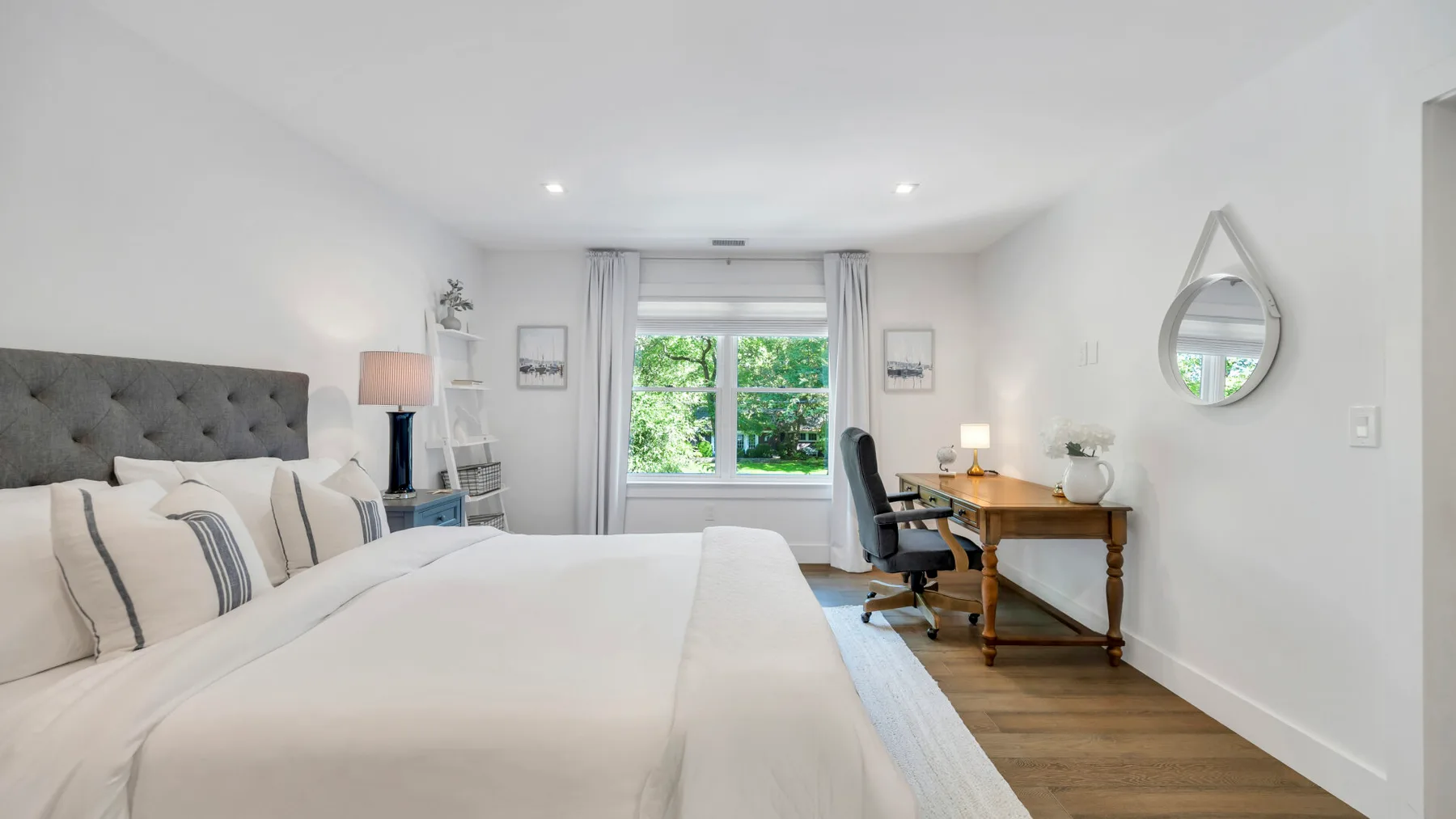 Un dormitorio luminoso con una cama grande y un escritorio junto a la ventana.