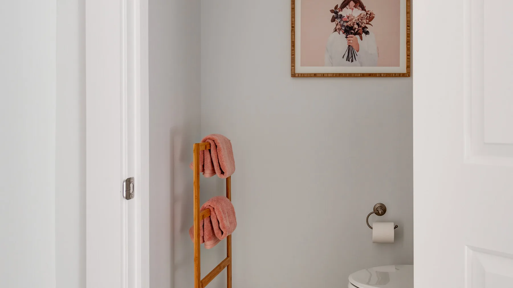 Una pared de baño tiene un toallero de madera y una lámina floral enmarcada.