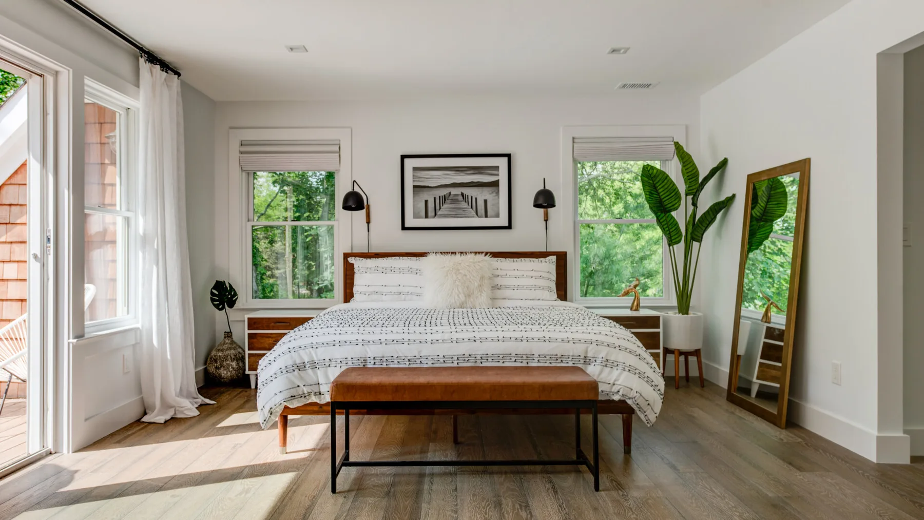 Un dormitorio luminoso con una cama bien tendida y grandes ventanas con vistas a la vegetación.