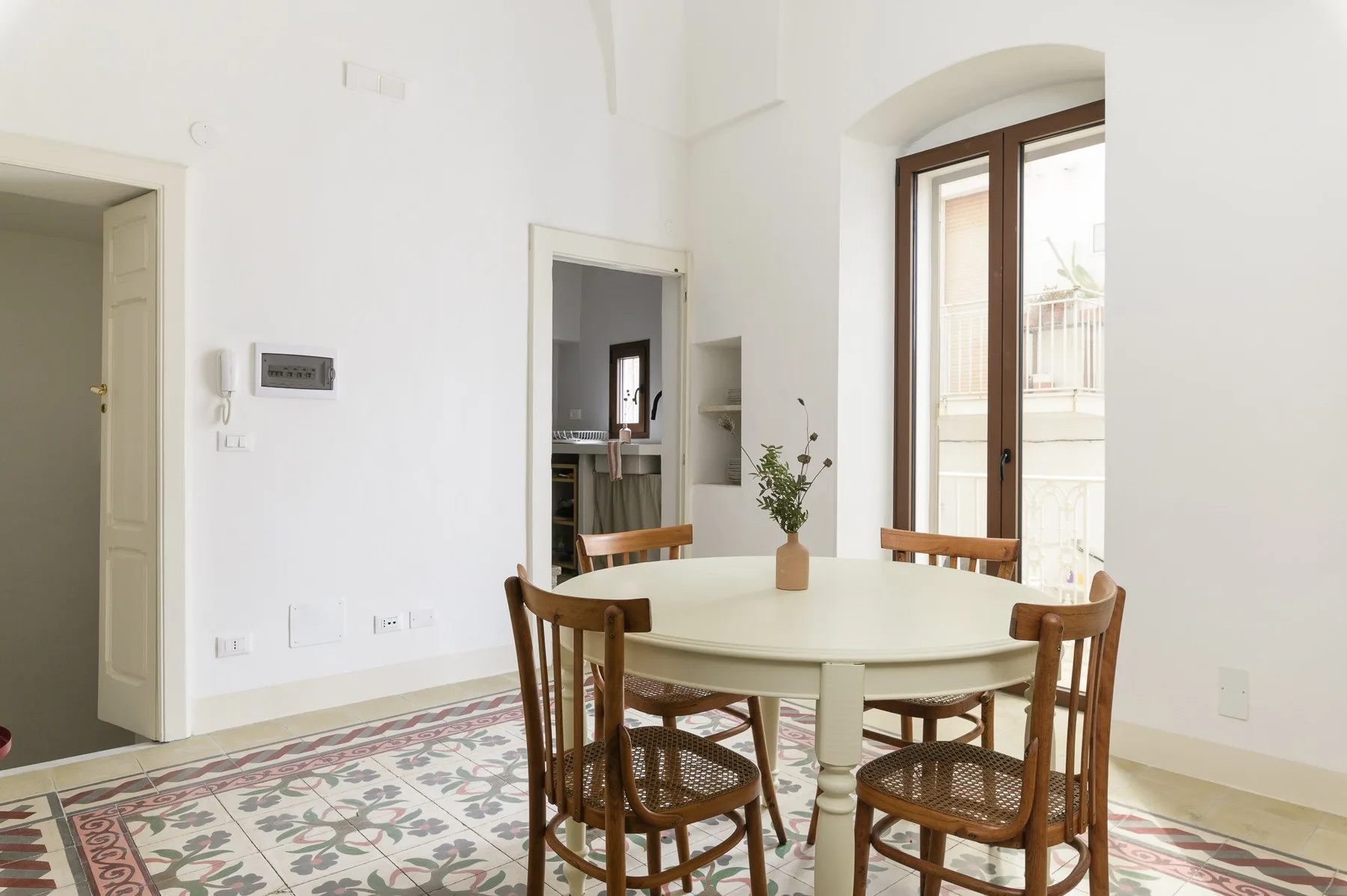 A bright dining area with a round table and wooden seating beside tall windows.