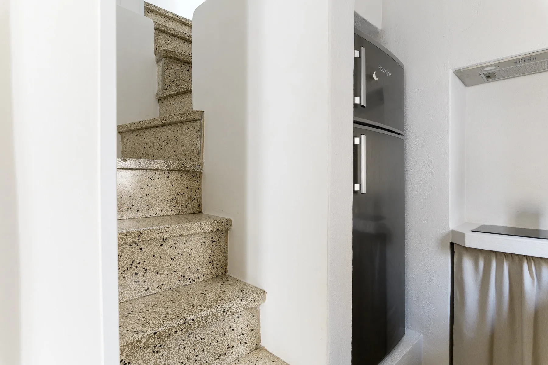 A compact kitchen with a refrigerator beside a staircase.