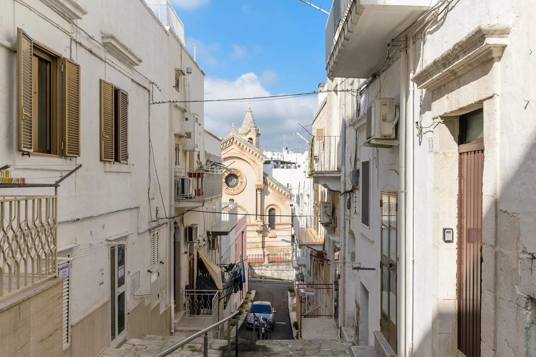 A narrow street runs between white buildings toward a church with a circular window.