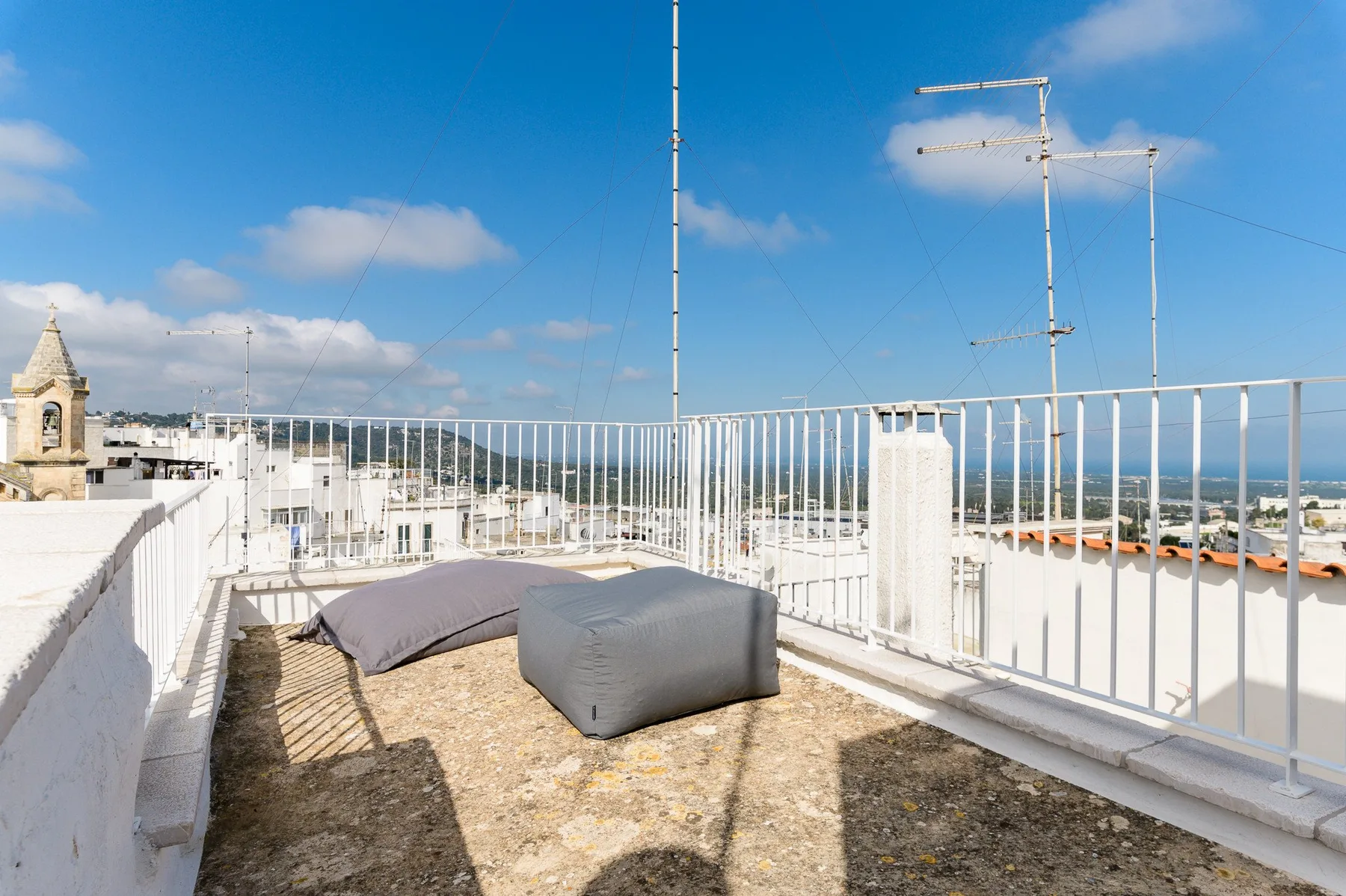 A rooftop terrace with outdoor seating and white railings under a blue sky.