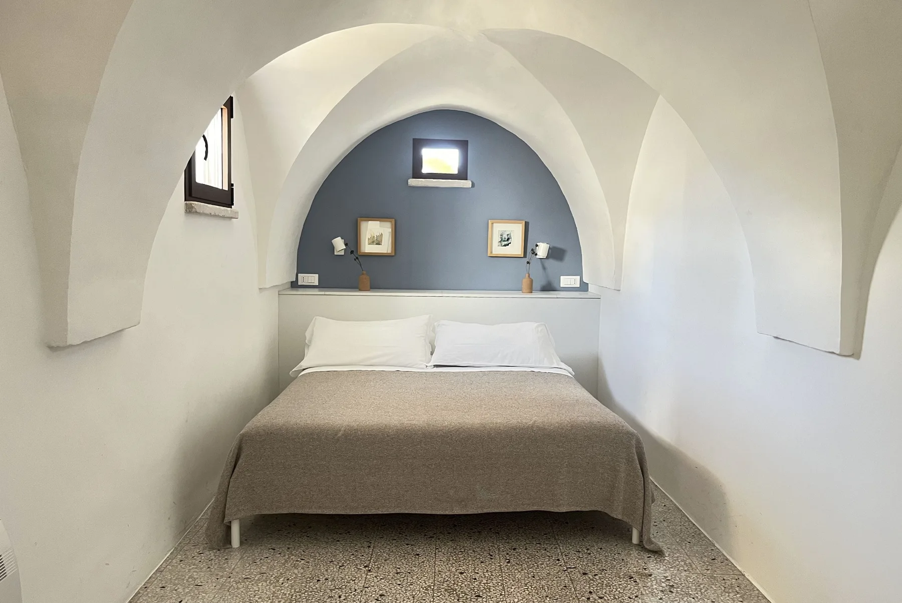 A bedroom with a bed beneath an arched alcove and framed pictures.