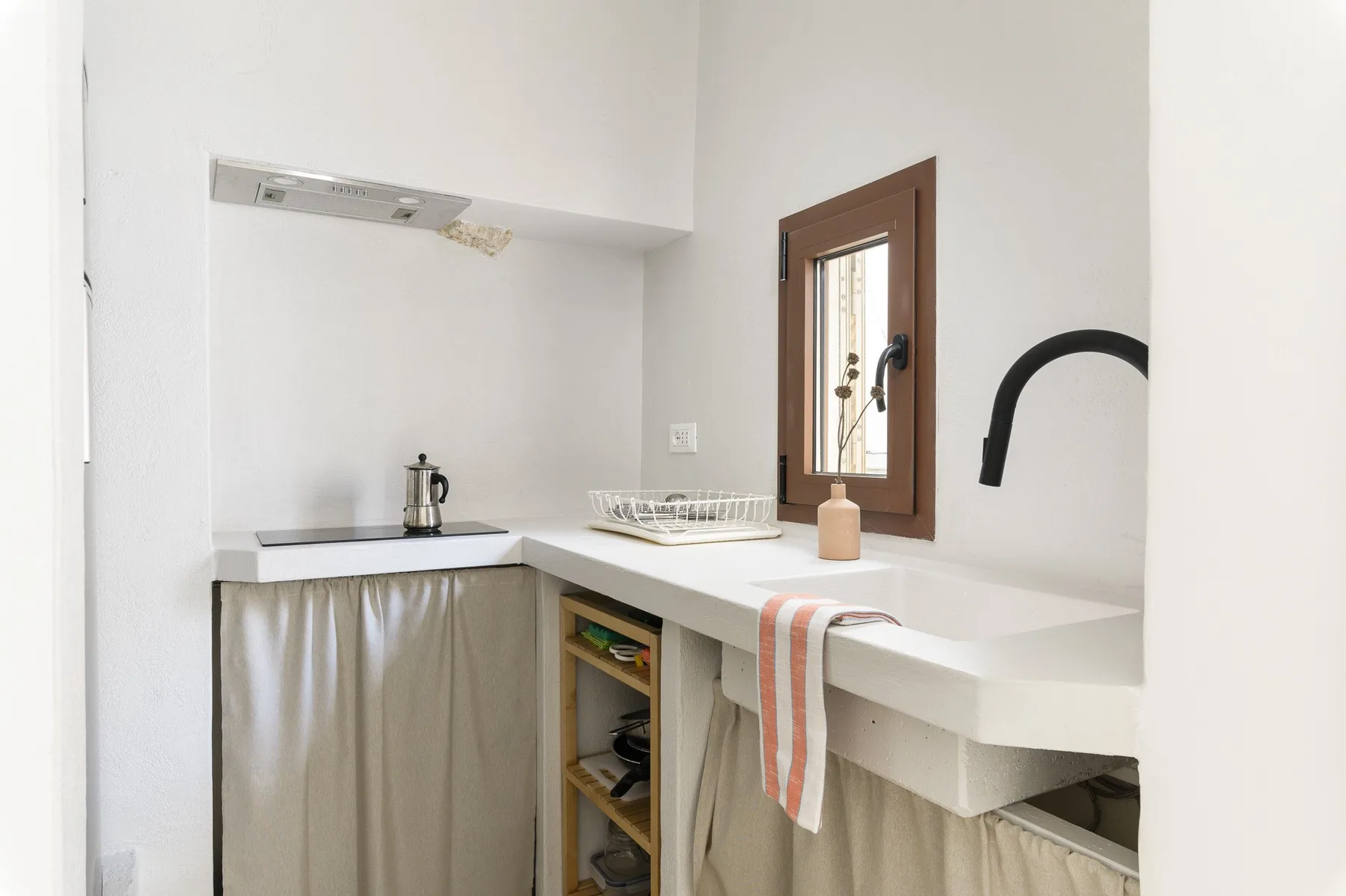 A compact kitchen with white counters, a sink, and a small window.