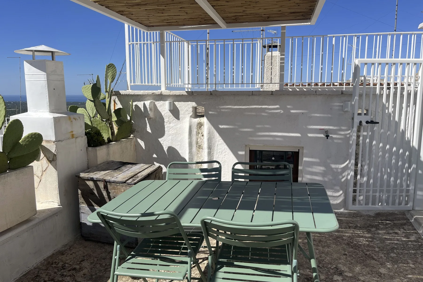An outdoor patio with a green table and seating beneath a pergola.